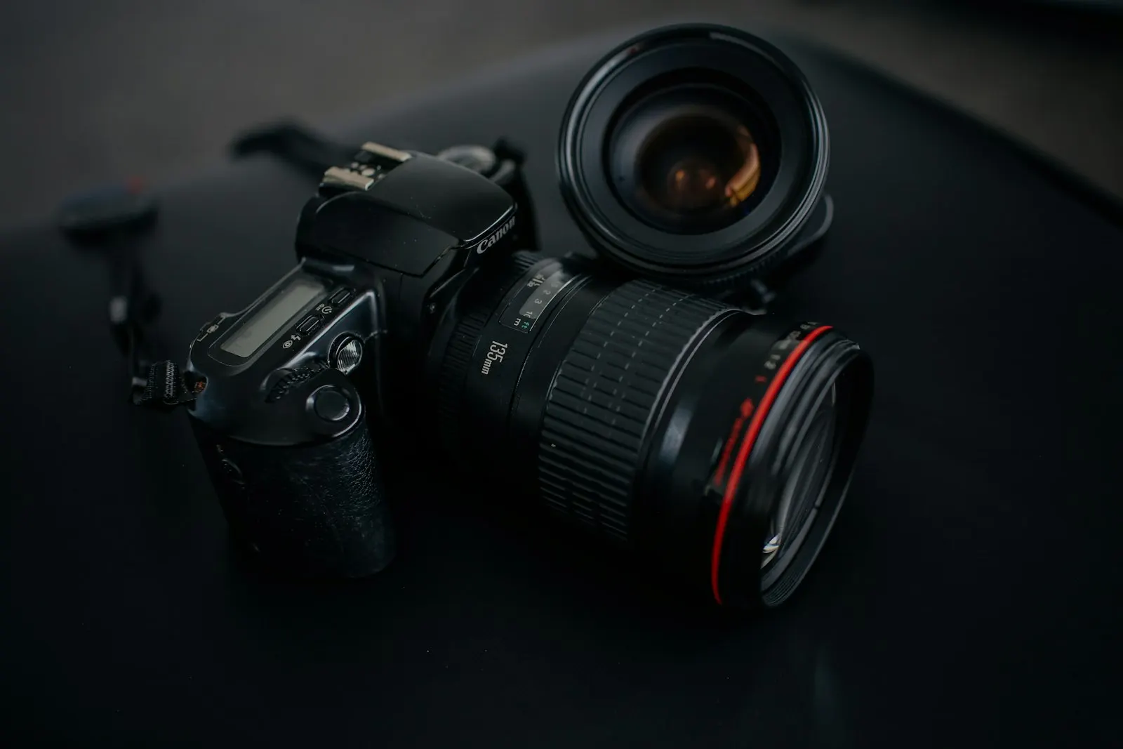 Canon DSLR camera body beside a camera lens on a black surface