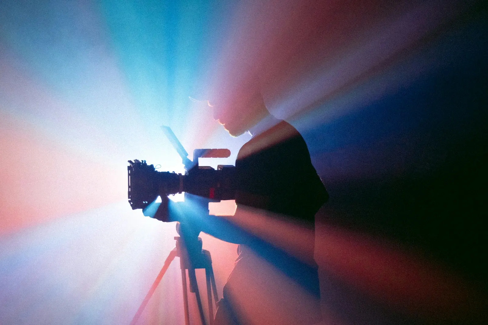 Silhouette of a camera operator behind a cinema camera, lit by blue and red light